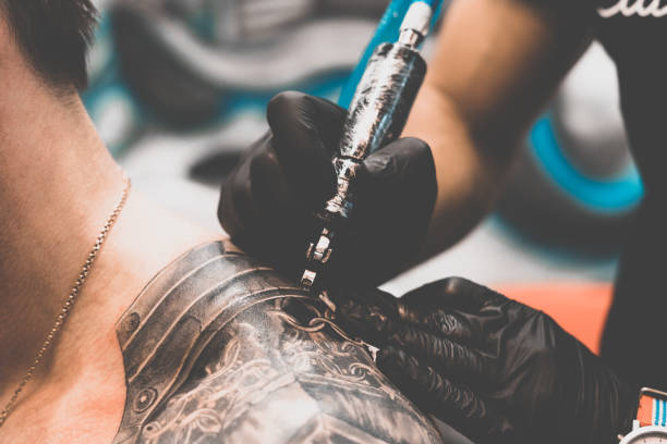 tattoo-salon. der tätowierer tätowiert einen mann auf seine schulter. tattoo-maschine, sicherheit und hygiene bei der arbeit. nahaufnahme, getönt, tätowierer - 5412 stock-fotos und bilder