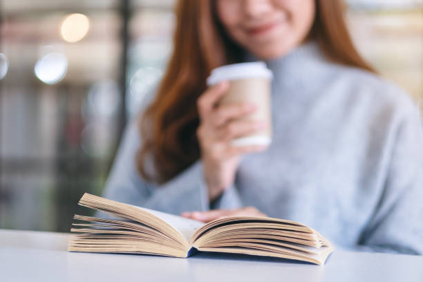 istock a woman holding and reading a book while drinking coffee on wooden table 1189844268