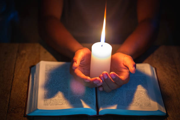 istock prayer - candle in hands, open bible, Religious concepts 1189846206