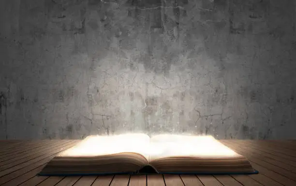 Photo of open illuminated big book on wooden floor