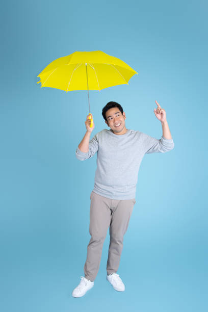 homem asiático feliz que prende o guarda-chuva amarelo no fundo azul. - cold rain parasol gray - fotografias e filmes do acervo