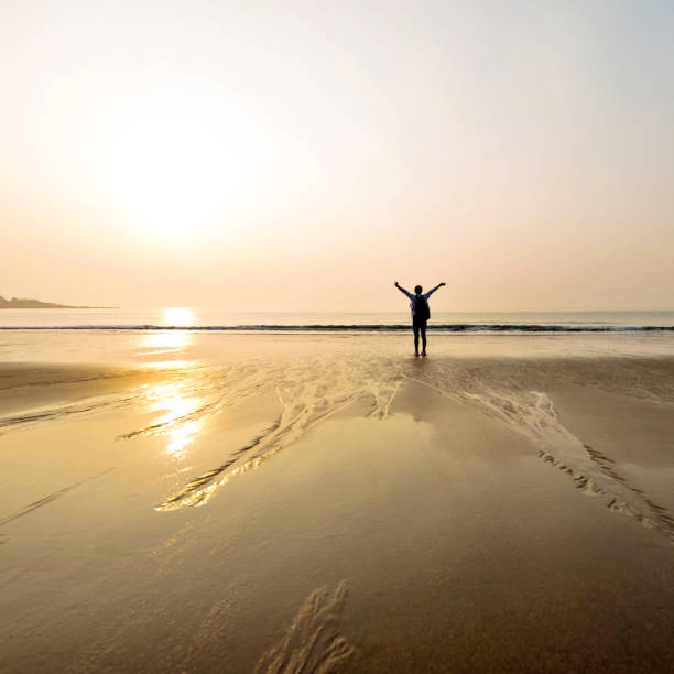 istock Woman backpacker standing on beach with arms raised 1189858549