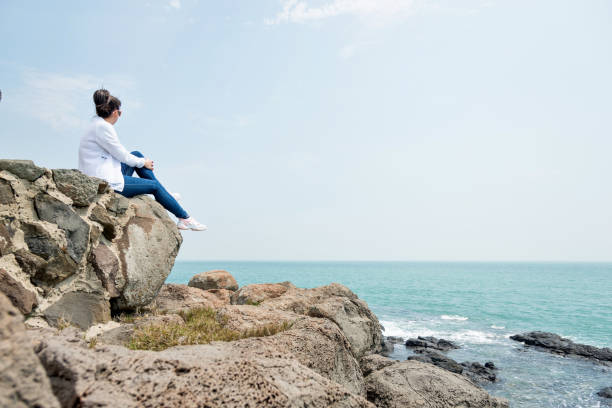 istock Woman sitting on the rock by beach 1189859519