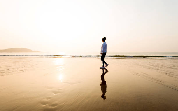istock Woman walking on the beach at sunset 1189859640