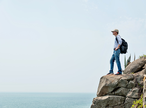 Man backpacker standing on the cliff by sea.