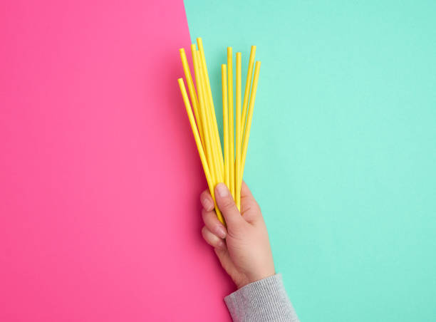 hand holds a stack of yellow paper tubes for a cocktail on a multi-colored background