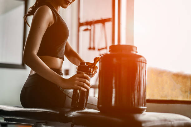 relaks po treningu.piękna młoda kobieta patrząc daleko siedząc na gym.young kobieta na siłowni robi sobie przerwę od workout.woman parzenia koktajlu białkowego. - athleticism zdjęcia i obrazy z banku zdjęć