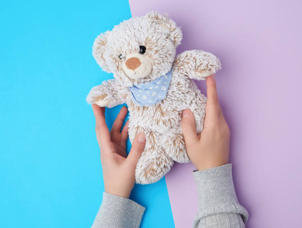 istock two female hands hold a small toy teddy bear on a blue background 1189876210