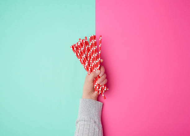 hand holds a stack of red paper tubes for a cocktail on a multi-colored background