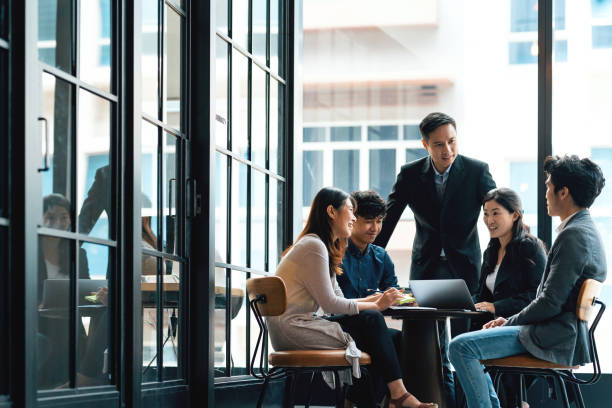 Young creatives and team leader in discussion in an open working environment Young creatives and team leader in discussion in an open working environment southeast asia photos stock pictures, royalty-free photos & images