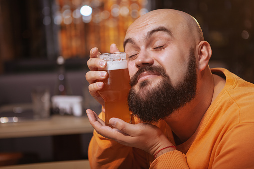 Close up of a happy bearded man cuddling with a glass of beer. Cheerful man loving his beer