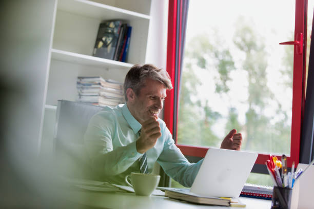 istock Mature businessman smiling while reading email on his laptop in office 1189888268