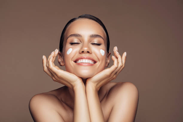beautiful woman applying cream on her face - beauty treatment skin care beauty young women imagens e fotografias de stock