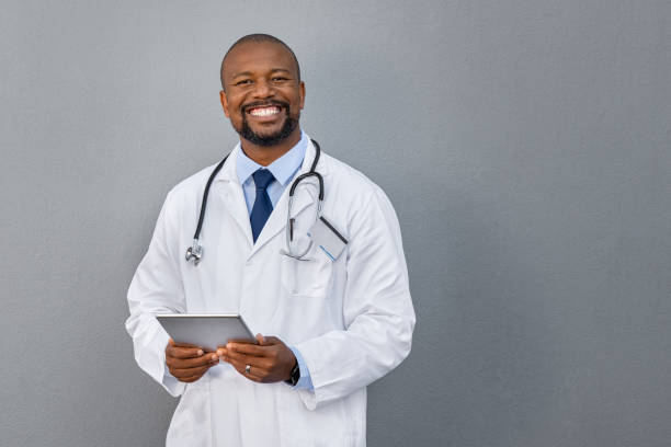 회색 벽에 서있는 미소 짓는 의사 - doctor male doctor mature men portrait 뉴스 사진 이미지