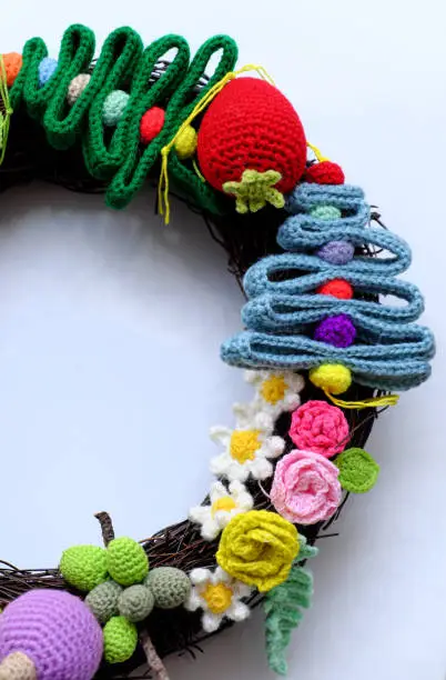 Amazing colorful Christmas wreath from handmade crochet product with multicolor yarn on white background, ornament  for garland from pine tree, flower, fruit, leaf, wonderful craft decoration