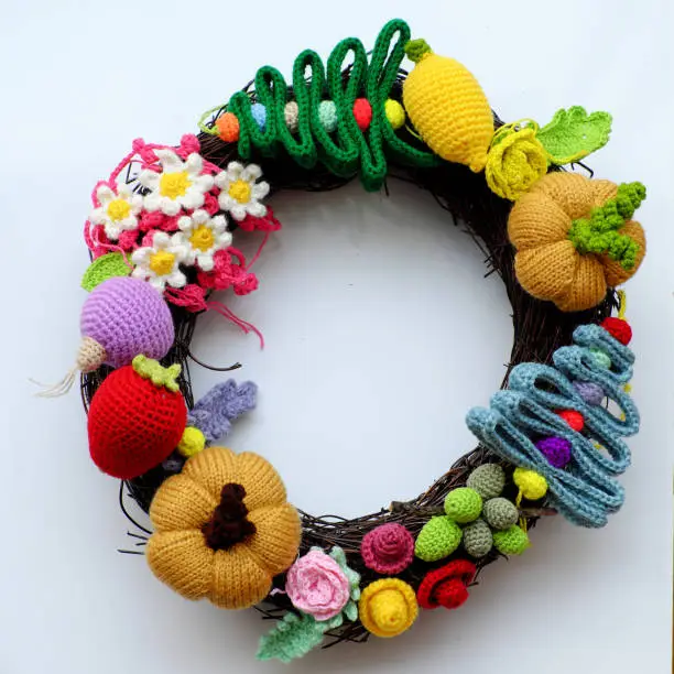 Amazing colorful Christmas wreath from handmade crochet product with multicolor yarn on white background, ornament  for garland from pine tree, flower, fruit, leaf, wonderful craft decoration