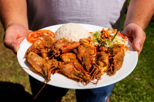 istock A man holds a plate with tiger prawns, a side dish and salad. 1189904909