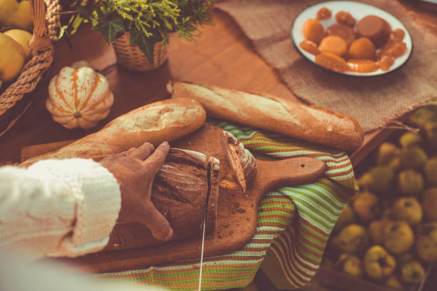 Close up of senior woman cutting bread with knife on a cutting board.