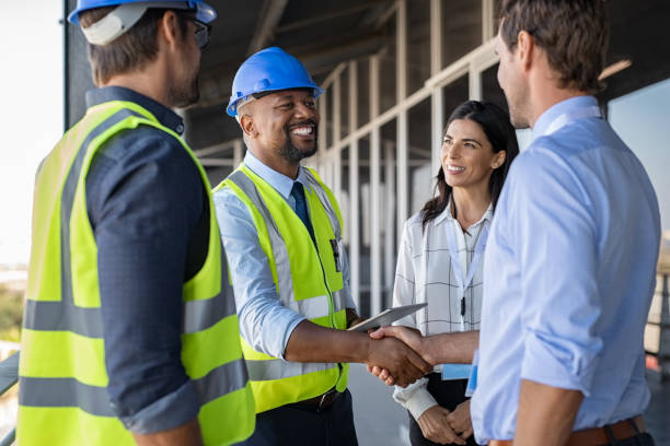 Engineer and businessman handshake at construction site Smiling engineer shaking hands at construction site with happy architect. Handshake between cheerful african construction manager with businessman at bulding site. Team of workers with architects and contractor conclude an agreement with safety uniform. maintenance worker stock pictures, royalty-free photos & images