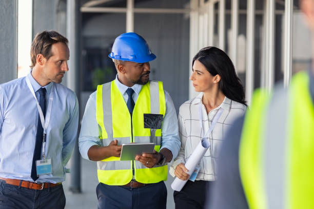 Engineer and architects at construction site Team of construction workers discussing project details with executive supervisor holding blueprints and digital tablet. Team of architects and civil engineers inspecting construction site. Structural african engineer and architect with work vests discuss the construction process. african american architecture stock pictures, royalty-free photos & images