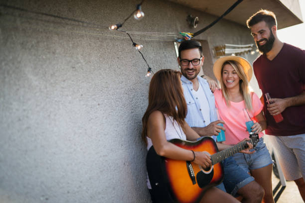 istock Young friends having fun at a rooftop party, playing the guitar, singing, dancing and drinking 1189916509