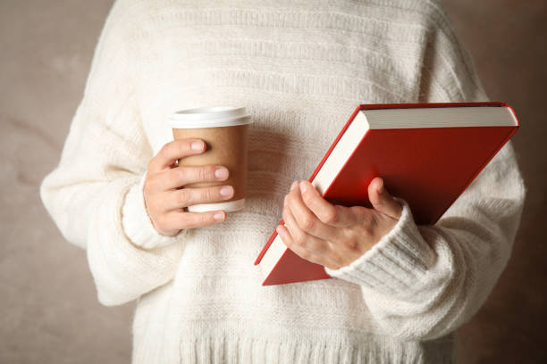 istock Woman holding book and coffee against brown background, front view 1189917948