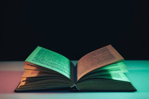 istock Beautiful open old book in the color light on a table and night background. 1189917982