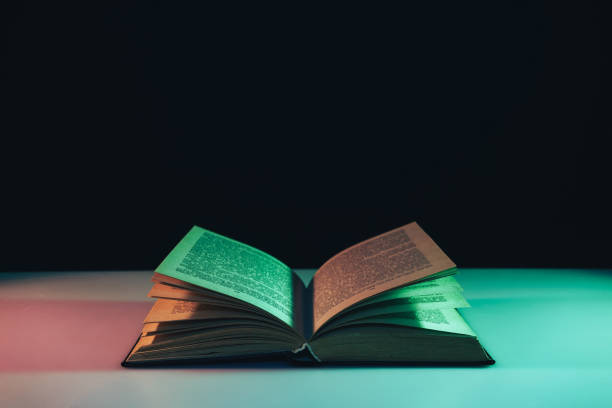 istock Beautiful open old book in the color light on a table and night background. 1189918009