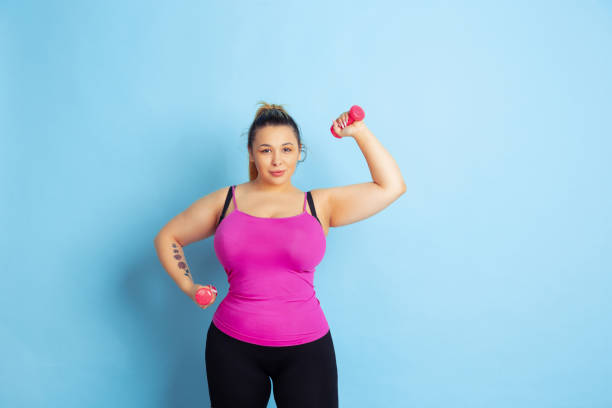 istock Young caucasian plus size female model's training on blue background 1189918124