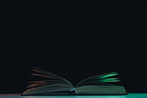 istock Beautiful open old book in the color light on a table and night background. 1189918174