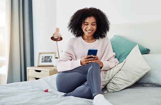 Cropped shot of an attractive young woman sitting on her bed and using her cellphone at home