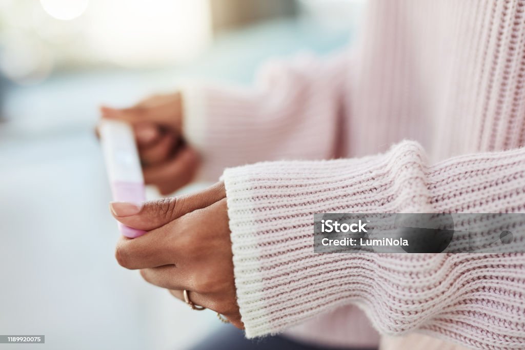 How long do I have to wait? Cropped shot of an unrecognizable woman sitting on her bed alone and waiting for a pregnancy test result at home Pregnancy Test Stock Photo