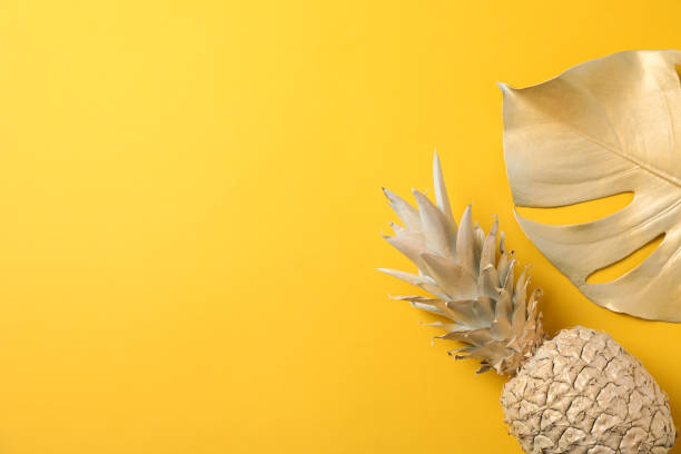 istock Painted gold pineapple and palm leaf on yellow background, space for text 1189922688