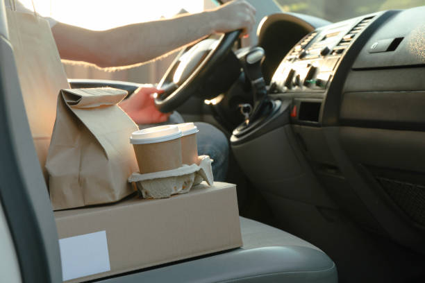 istock Blank box, coffee cups, paper packages and courier in car. Delivery 1189923303
