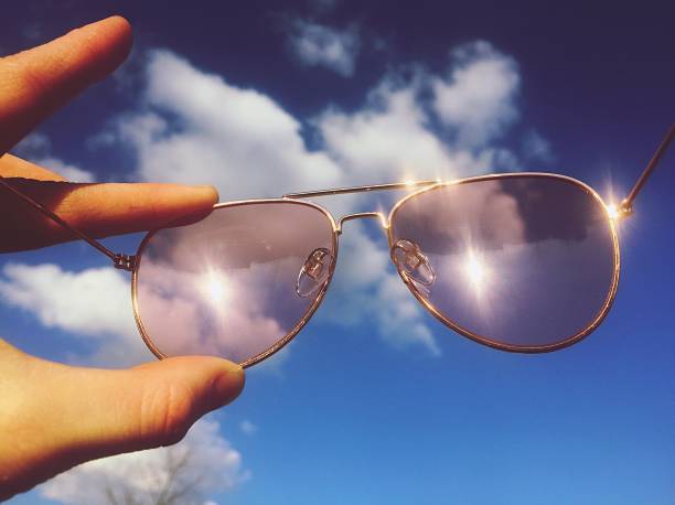 Hand holding pair of sunglasses against a sky.