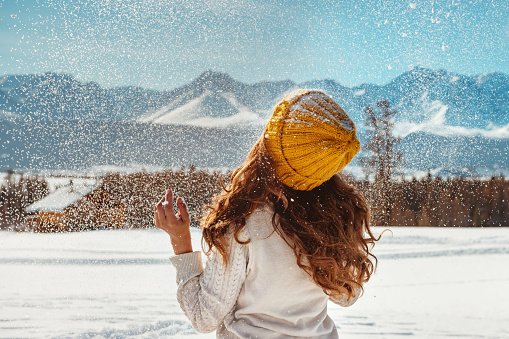Beautiful girl tossing snow against mountains