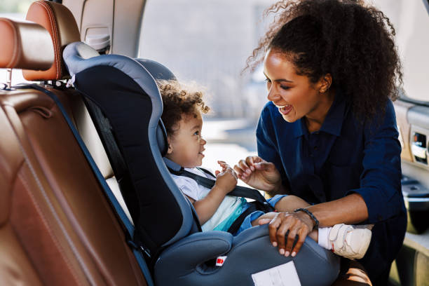 buona madre che guarda suo figlio in un seggiolino. giovane ragazza che prepara il bambino per un viaggio. - laccio foto e immagini stock