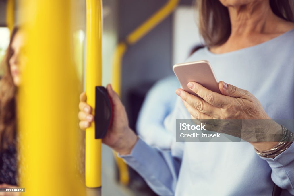 Woman using smart phone in bus Midsection of senior woman using smart phone in bus. Female is text messaging while commuting by public transport. She is in casual. Bus Stock Photo