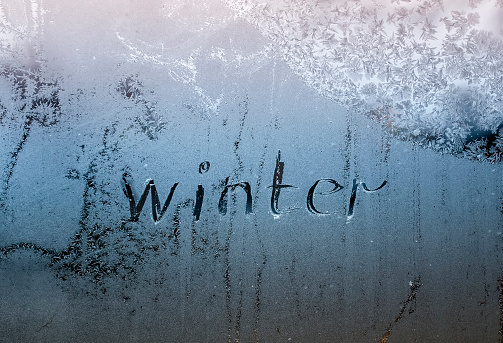 text word winter scraped on frosty glass covered with white frost crystals on window on winter cold clear morning