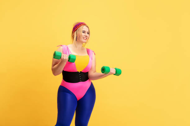 istock Young caucasian plus size female model's training on yellow background 1189932942