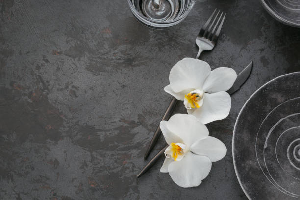 istock Elegance table setting with knitted grey napkin, cutlery, ceramic plates, glasses and white orchid flowers 1189935112
