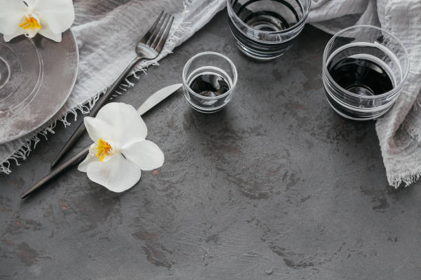 Elegance table setting with knitted grey napkin, cutlery, ceramic plates, glasses and white orchid flowers