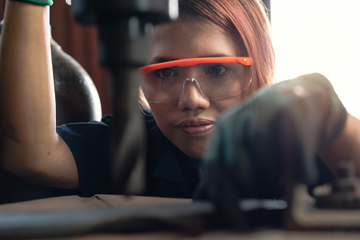 Joven mujer diversa concentrándose mientras opera la máquina de perforación industrial photo