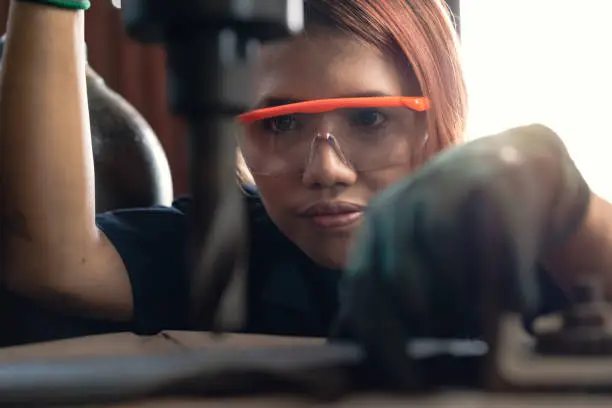 Photo of Young diverse woman concentrating while operating industrial drilling machine