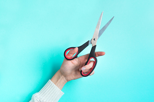 Hand holding Scissors, blue background with copy space. Minimal trendy composition.