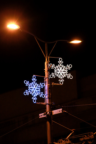 Christmas blue and white lights simulating shape of frozen snowflakes. Street detail of New Year and Christmas decorations, string rice lights bulbs. Ornaments to christmas celebration, holiday scene.