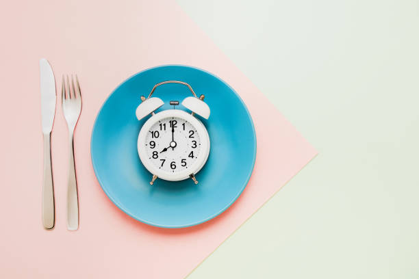 istock Intermittent fasting concept. White alarm clock on empty blue plate. Top view, copy space 1189947608