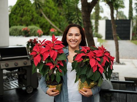 A mexican mother carrying red christmas flowers outside and smiling away.