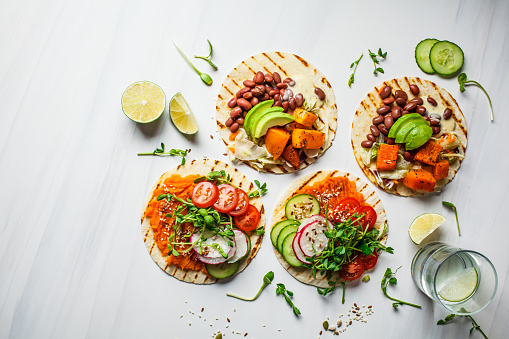 Open vegan tortilla wraps with sweet potato, beans, avocado, tomatoes, pumpkin and seedlings on a white background, top view, flat lay. Healthy vegan food concept.