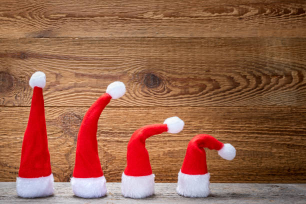 Four red Christmas hats on a wooden table against a wooden background